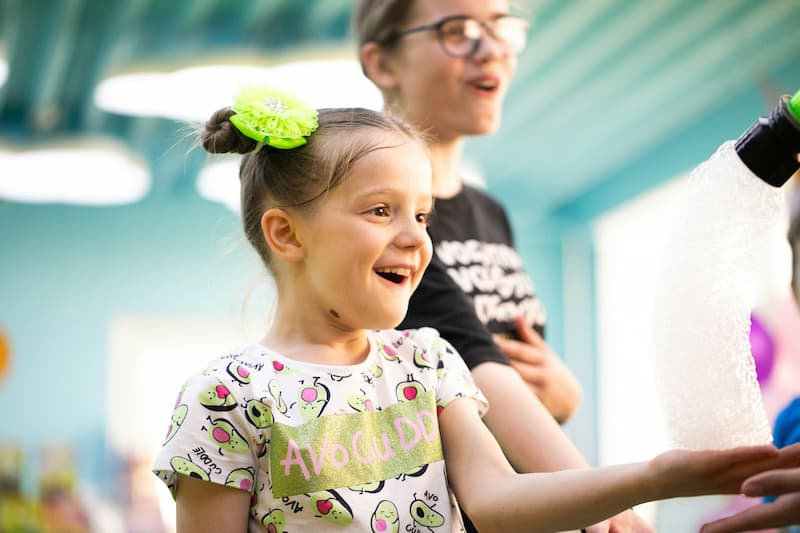 A young girl smiling, holding something in her hand.