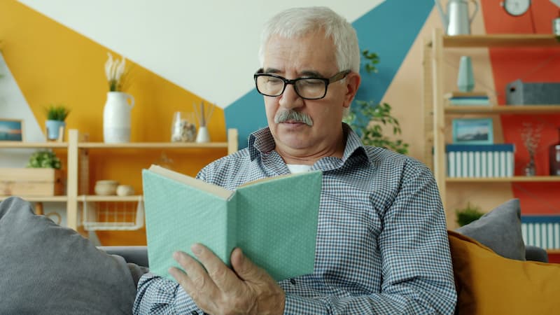 An older man wearing glasses, reading a book.